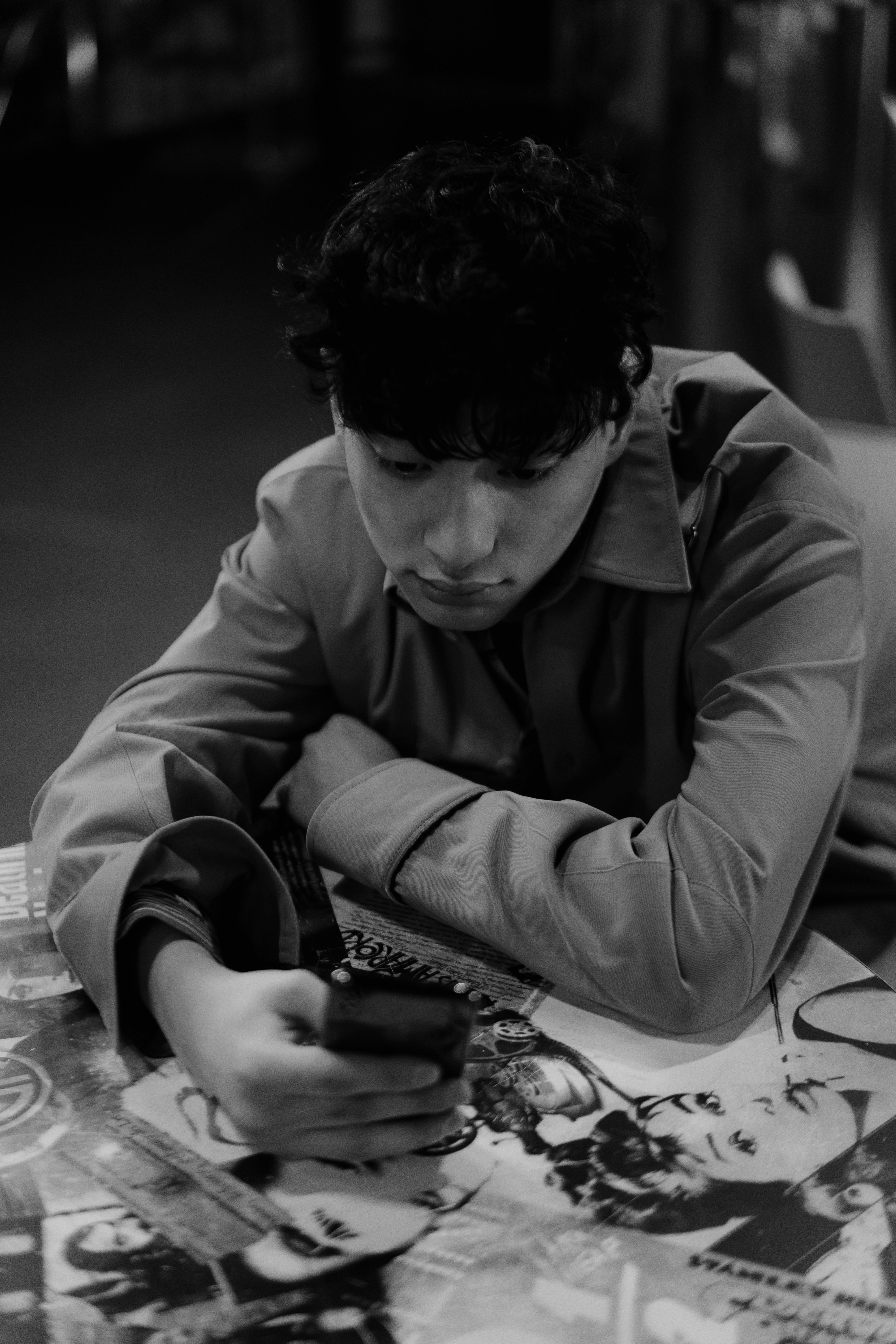 A man leaning over a table, absorbed in his phone, surrounded by others but disconnected