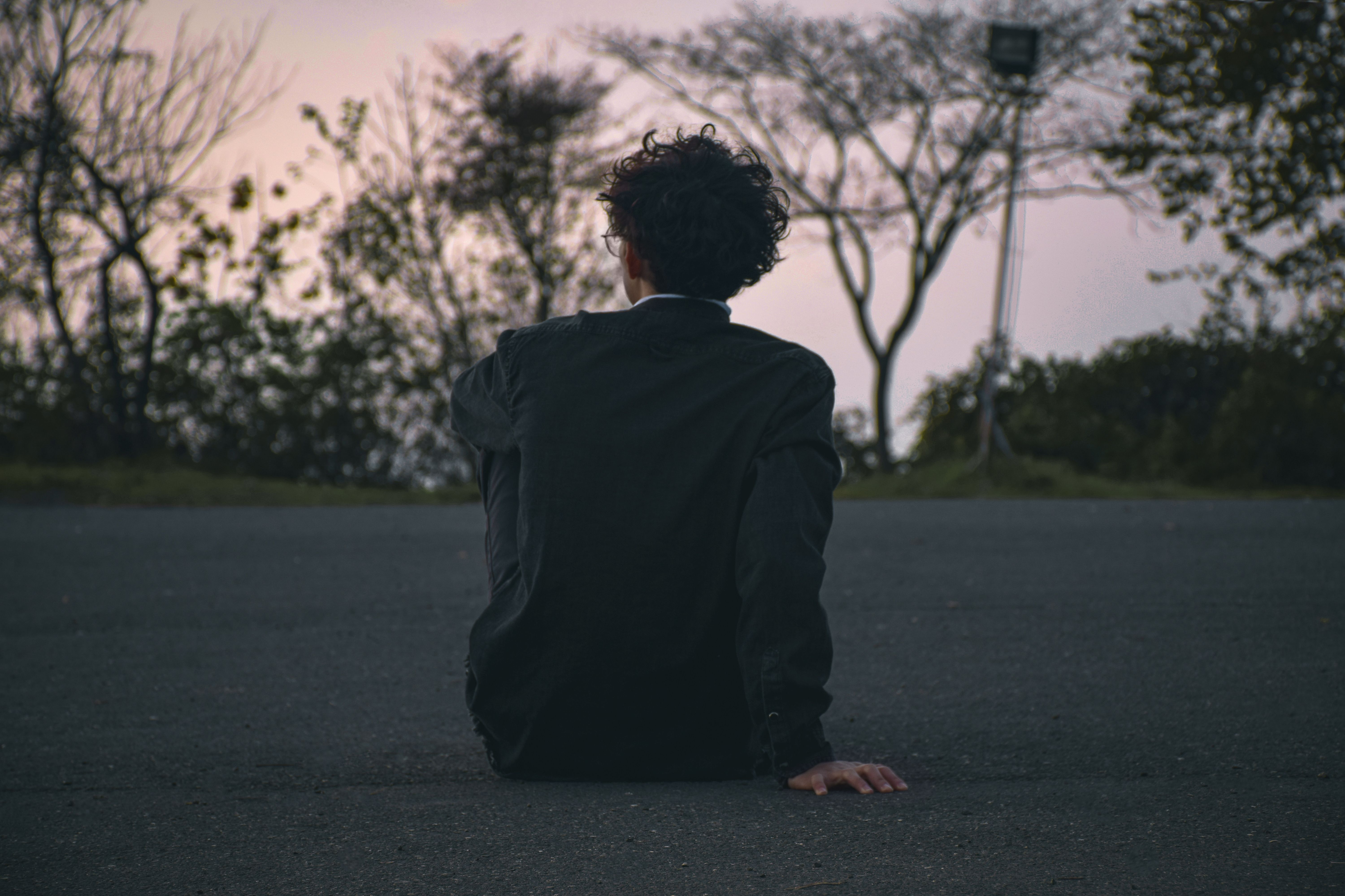 A man sitting alone at dusk, looking out toward the trees
